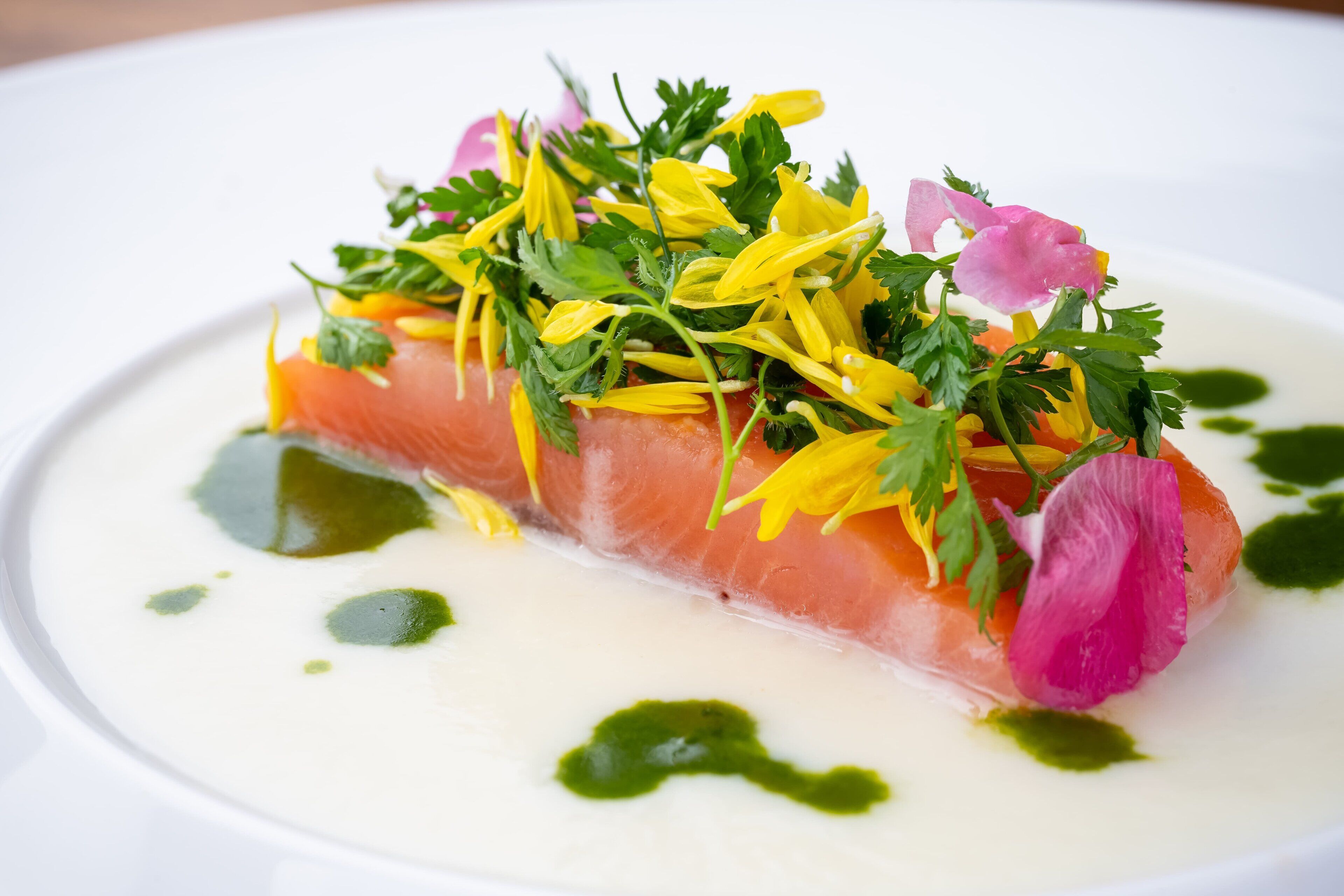 Ein Teller mit Lachs, Grünzeug und Blumen.