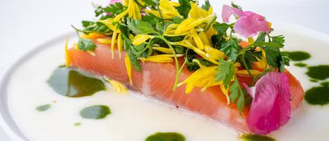 Ein Teller mit Lachs, Grünzeug und Blumen.