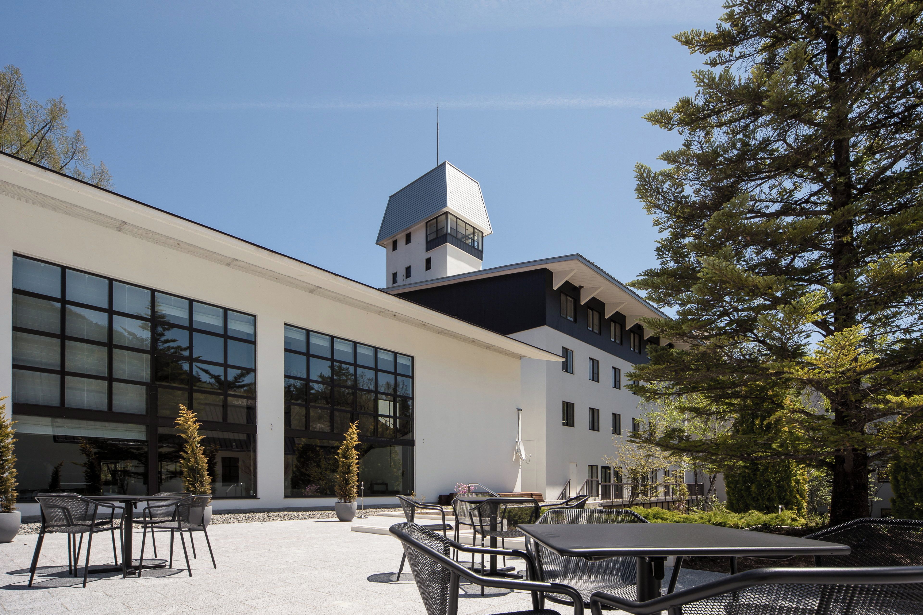 A modern building with a prominent tower, large windows, and outdoor seating area.
