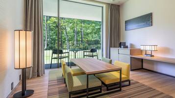 Ein modernes Hotelzimmer mit einer großen Schiebeglasdoor zum Balkon, einem Holztisch, einer Couch, einem Schreibtisch und einer Lampe.