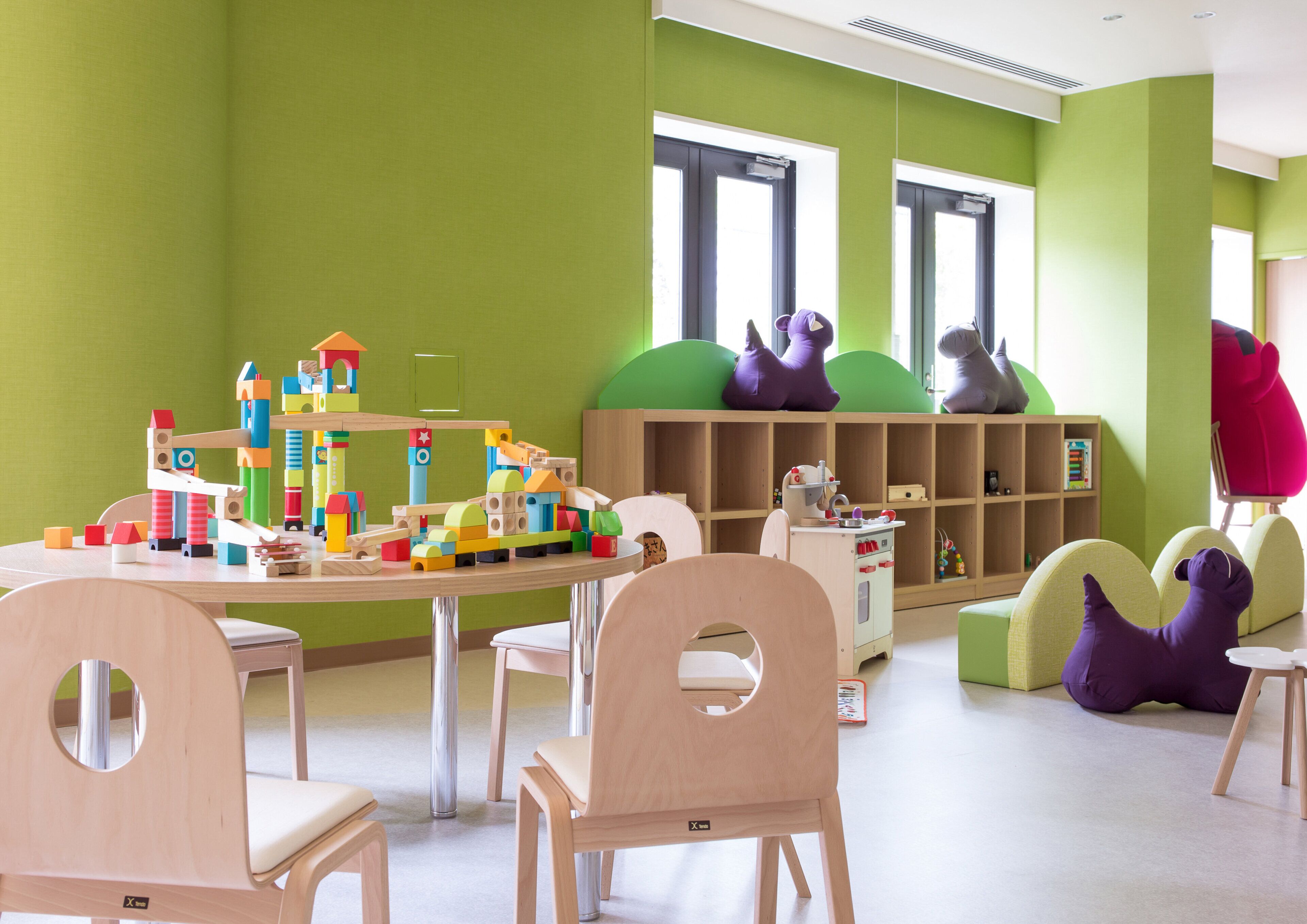 A children's playroom with a table of building blocks, chairs, and a bookshelf.