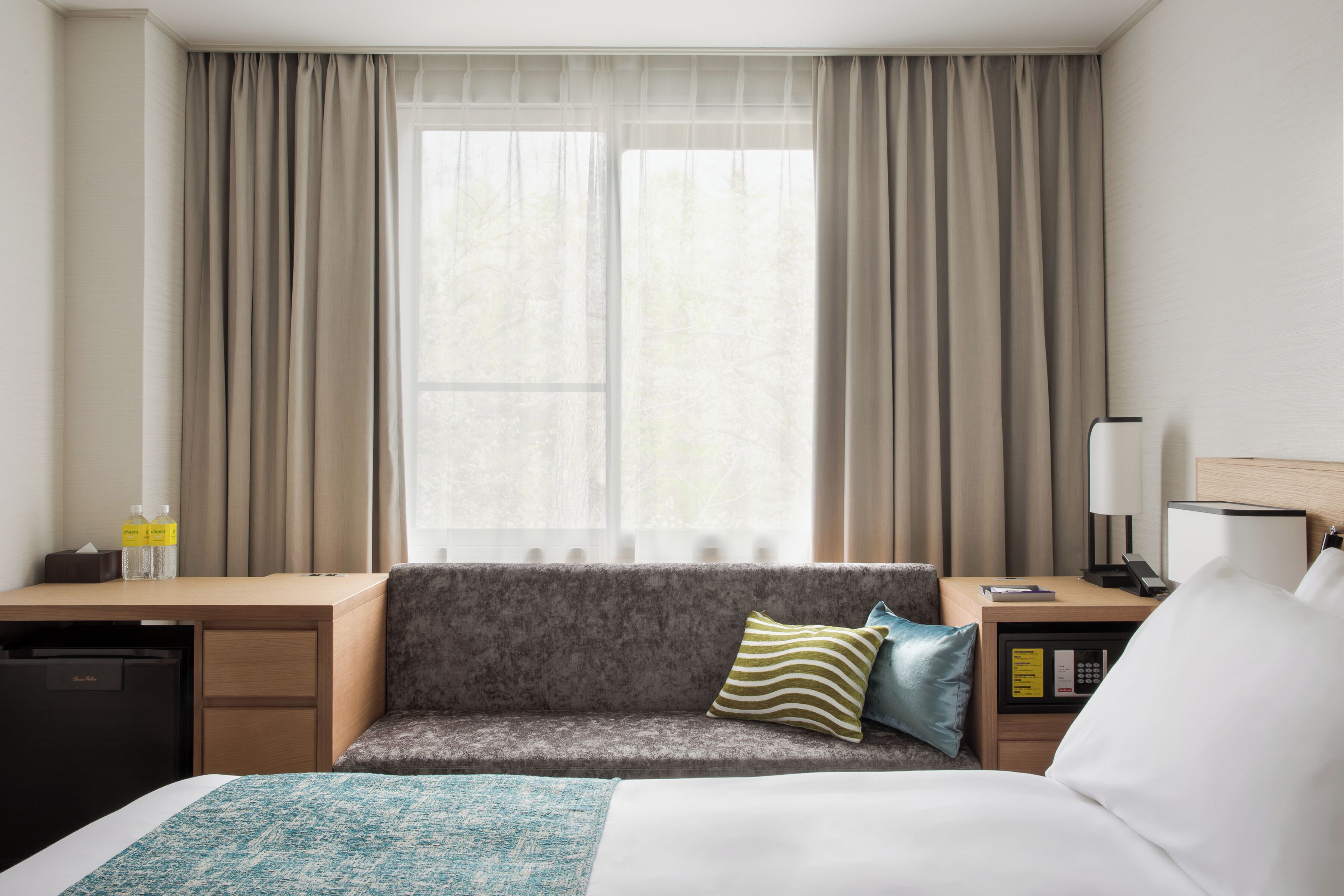 Ett hotellrum med en säng, en soffa, ett skrivbord, en lampa och ett fönster med gardiner.