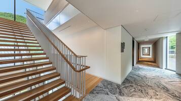 A modern interior with a wooden staircase, a marble floor, and a view through large windows.