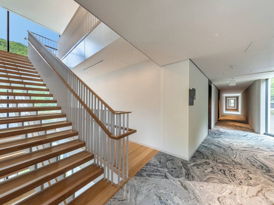 A modern interior with a wooden staircase, a marble floor, and a view through large windows.
