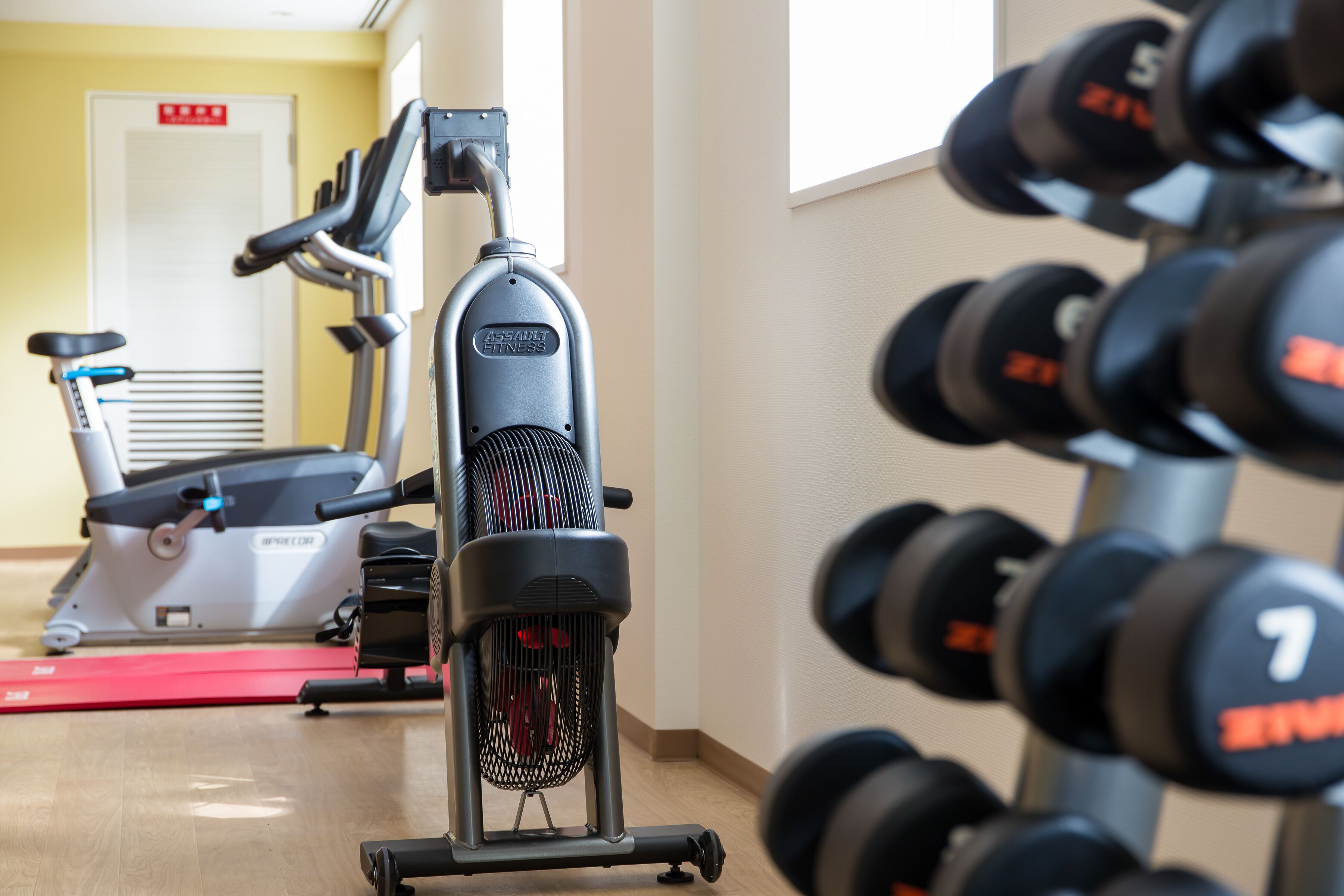Un gimnasio con equipo de ejercicio, incluyendo una bicicleta estática, elíptica y un estante de mancuernas.