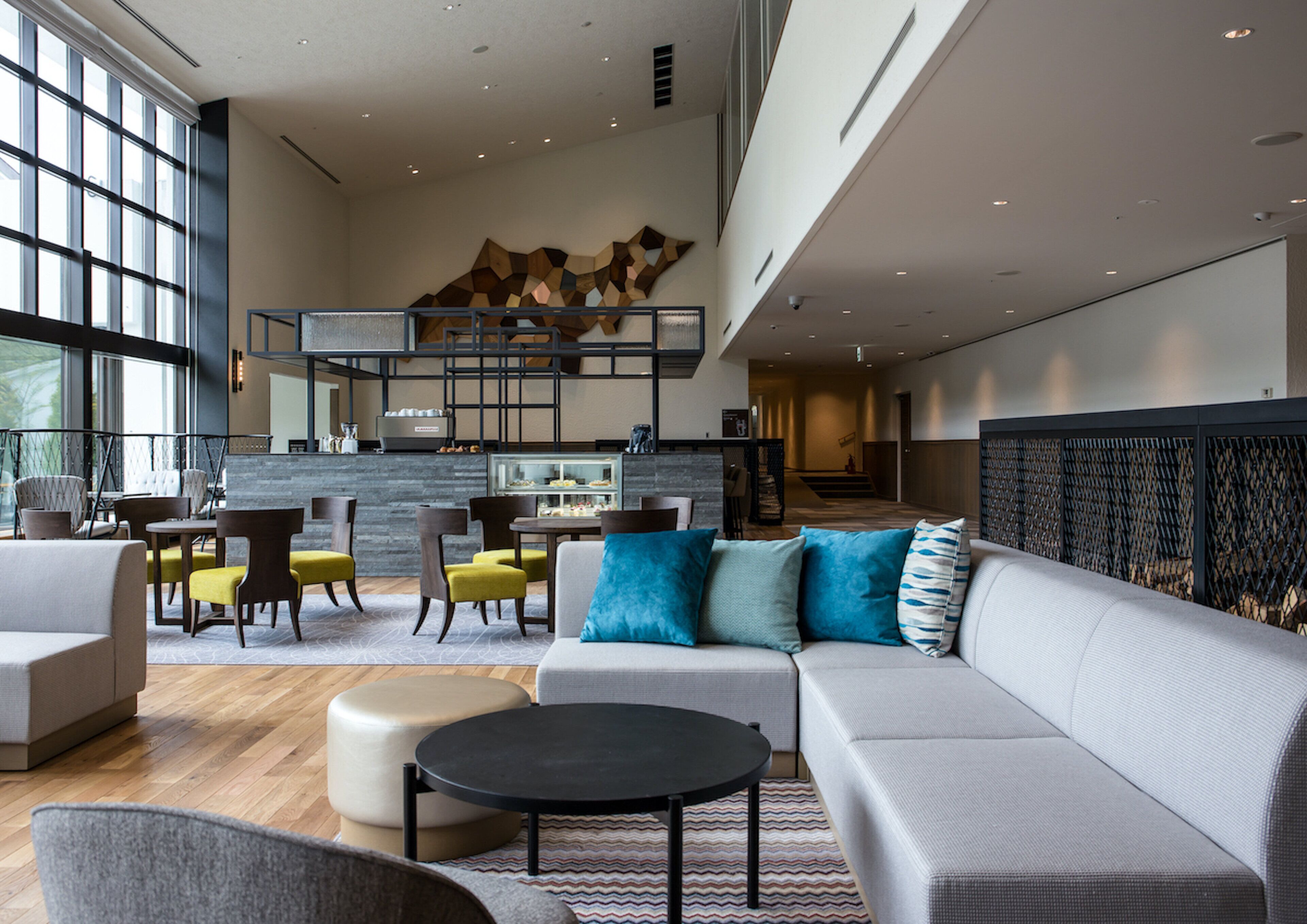 A modern living room with a sofa, coffee table, and chairs, a kitchen area with a counter and stools, and a staircase leading to an upper level.