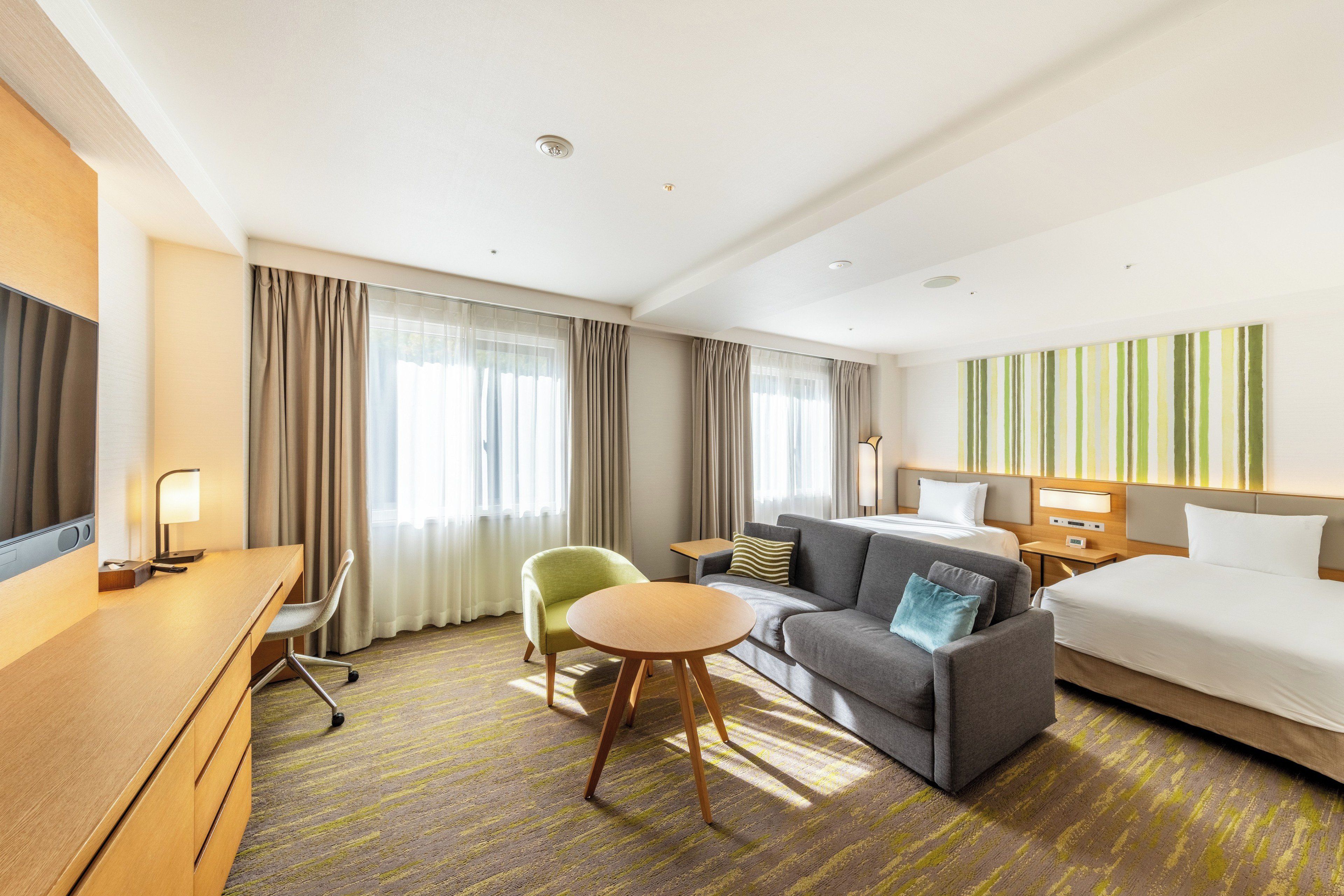 A hotel room with a bed, a sofa, a desk, a chair, and a small table.