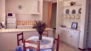 A compact kitchen with a microwave, coffee maker, and a dining table with chairs. There are shelves with decorative plates and a potted plant on the counter. - Detached 3-star village house overlooking the Durance river. (Thèze)
