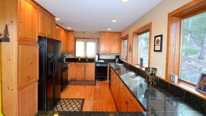 A modern kitchen with wooden cabinets, granite countertops, and a large window providing a view of the outdoors. - Morning Glory - 3 bedroom home - quiet wooded location (Estes Park)