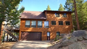 A two-story log cabin with a garage, a staircase to the upper level, and a natural setting with trees and rocks. - Morning Glory - 3 bedroom home - quiet wooded location (Estes Park)
