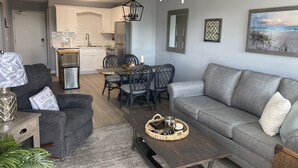 A modern living room with a grey sofa, a coffee table, and a dining area with a table and chairs. - Gulf Shores Plantation Resort by ALBVR (Gulf Shores)