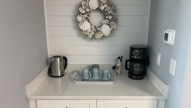 A kitchen counter with a kettle, coffee maker, and a tray of cups. - Gulf Shores Plantation Resort by ALBVR (Gulf Shores)