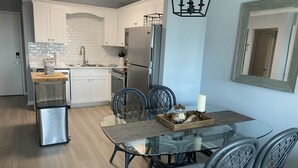 A modern kitchen with white cabinets, a stainless steel refrigerator, and a dining area with a glass table and chairs. - Gulf Shores Plantation Resort by ALBVR (Gulf Shores)