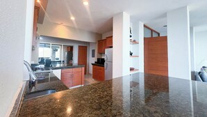 Une cuisine moderne dotée de plans de travail en granit, d’armoires en bois et d’un îlot central.