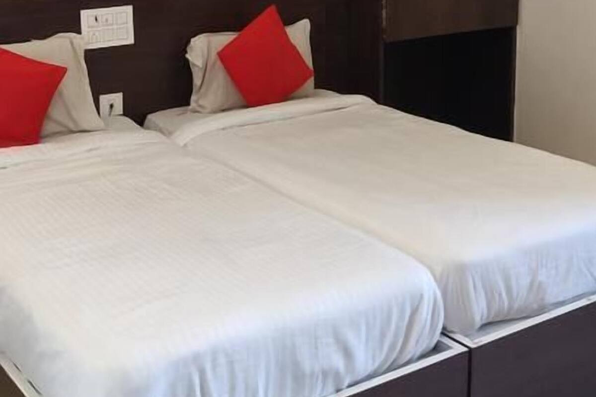 A double bed with white bedding and red pillows, a dark wooden wardrobe, and a ceiling fan.