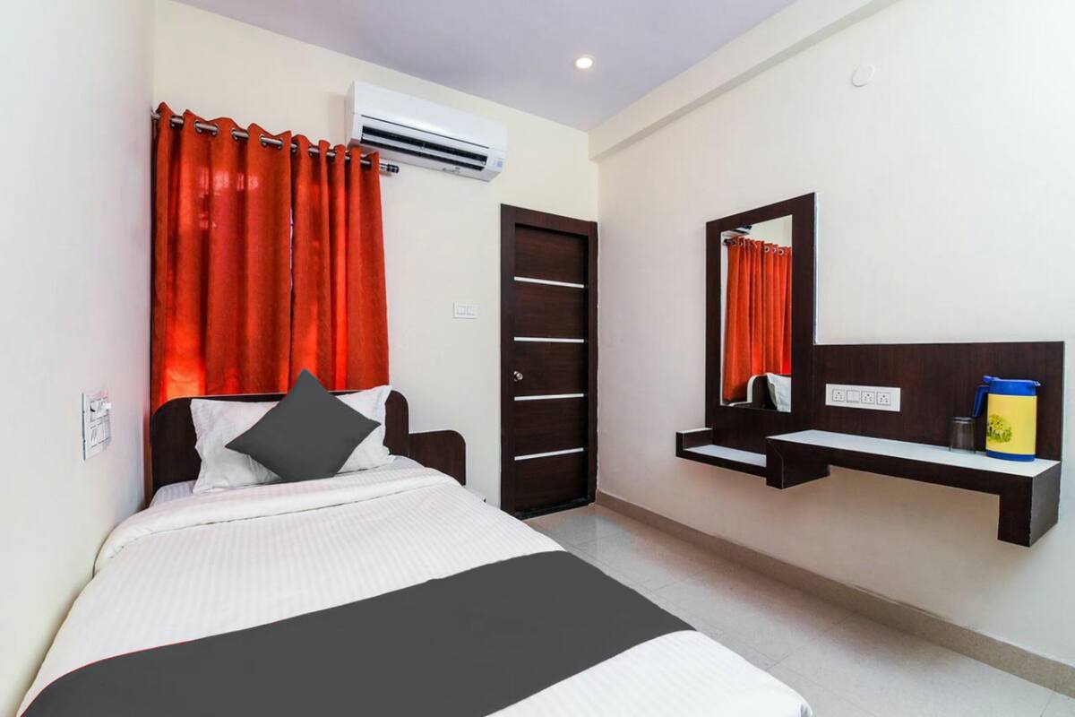 A hotel room with a bed, a nightstand, a mirror, and a shelf with toiletries.