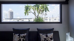 Ein modernes Wohnzimmer mit großem Fenster und Blick auf eine Stadtlandschaft, mit einer Couch, dekorativen Kissen und einem schlichten Beistelltisch.