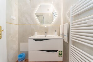 A modern bathroom with a white sink, a mirror with a hexagonal frame, and a towel rack.