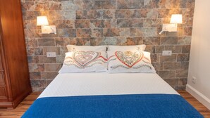 A bedroom with a stone wall, two bedside lamps, and heart-patterned pillows. - Quinta da Paz Madeira - Studio View Garden 4 (Caniço)