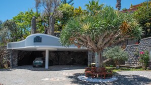 A modern building with a covered parking area, a stone wall, and a palm tree. - Quinta da Paz Madeira - Studio View Garden 4 (Caniço)