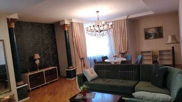 A living room with a green sofa, a coffee table, a chandelier, and a dining area with a table and chairs.
