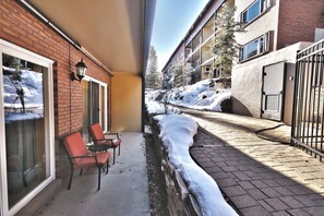 A narrow outdoor corridor with a brick building on one side and a gated area on the other, featuring a small seating area with chairs.