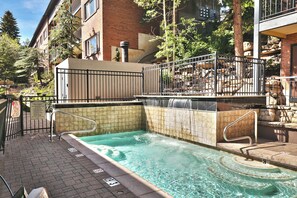 Una piscina con caída de agua, rodeada por un edificio de ladrillo y una valla metálica.