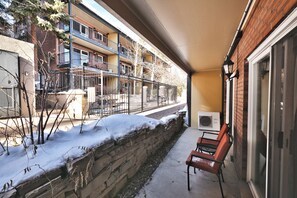 Un balcón con una silla, un muro de piedra y un edificio con varias ventanas y balcones.