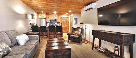 A living room with a wooden ceiling, a sofa, a coffee table, a TV, and a kitchen in the background.