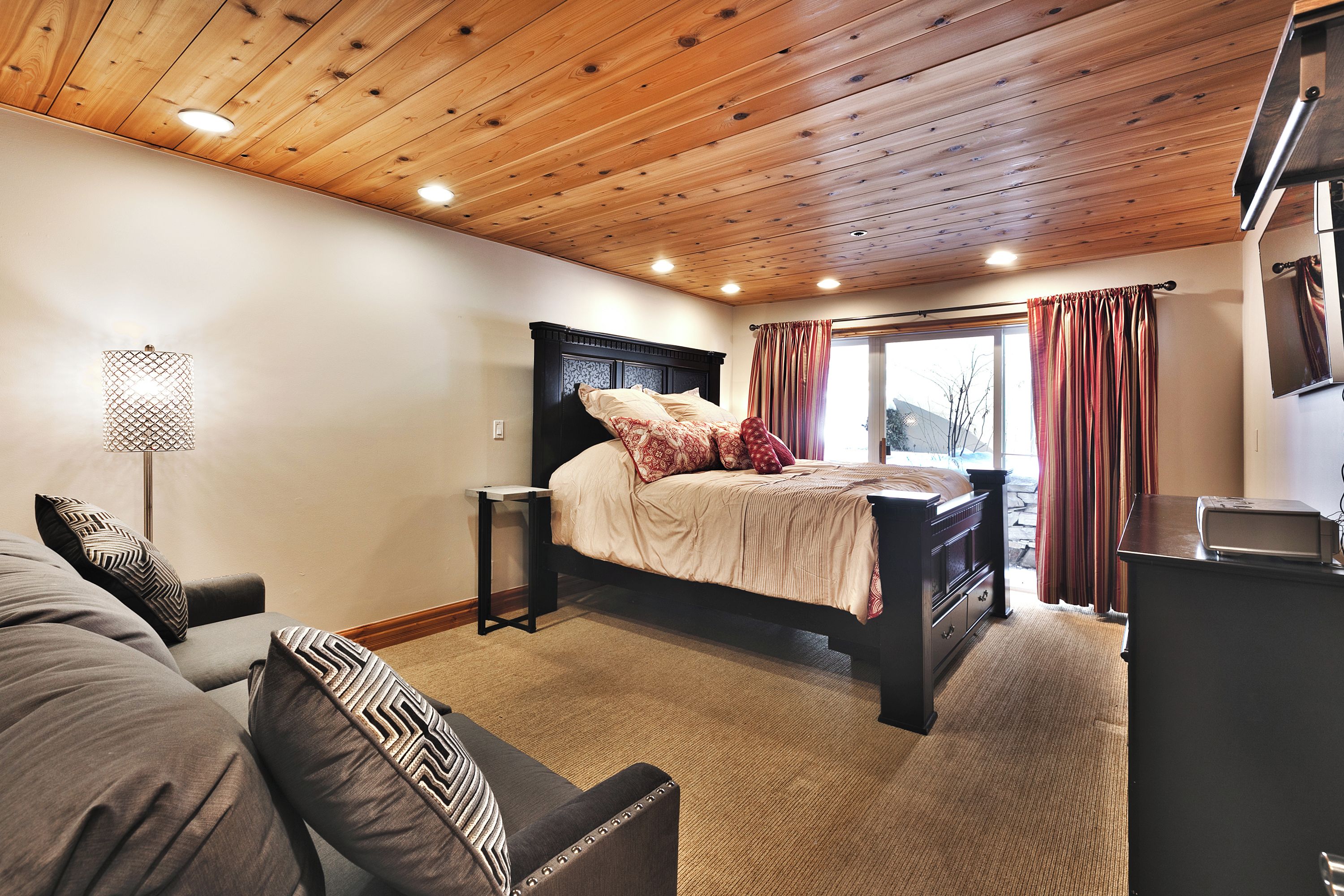 Ein Schlafzimmer mit Holzboden, einem Bett mit gemusterten Betttextilien, einem Nachttisch und einer Lampe.