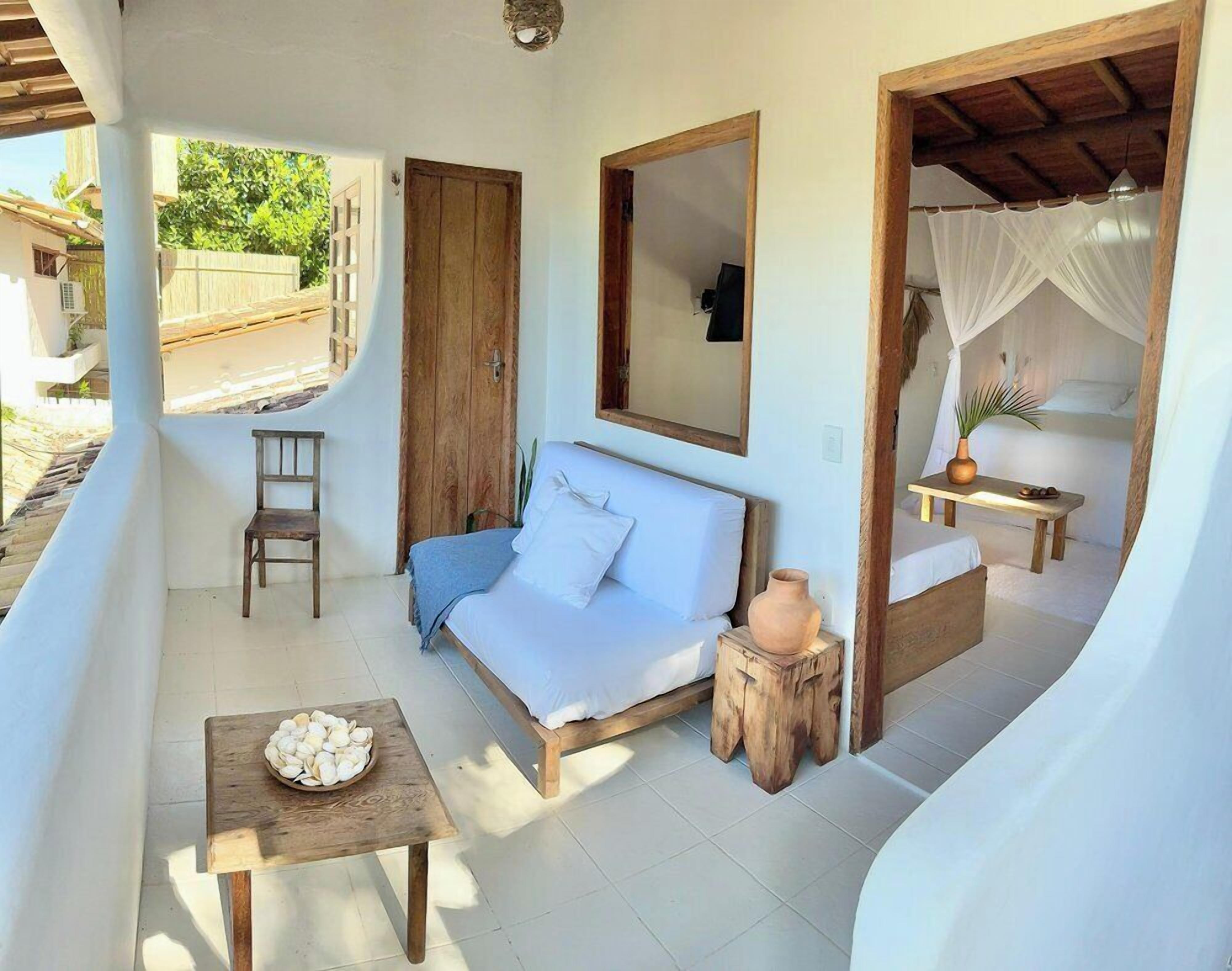 A cozy room with a bed, a wooden table with a bowl of fruit, a small stool, and a chair.