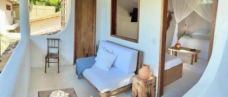 A cozy room with a bed, a wooden table with a bowl of fruit, a small stool, and a chair.