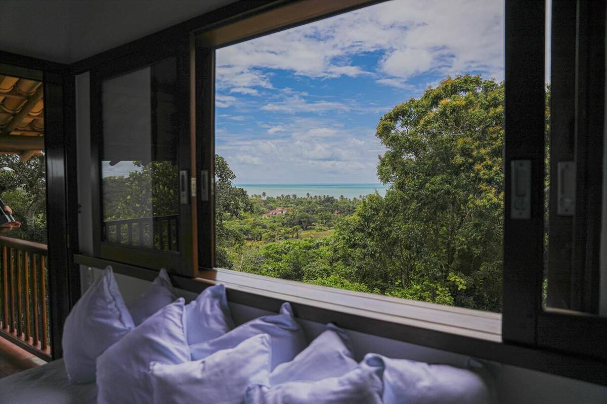 A room with a large window overlooking a lush landscape and a clear blue sky.
