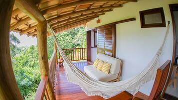 A hammock on a wooden balcony with a view of lush greenery.
