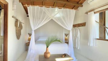 A room with a bed under a canopy, a small table with a vase and a shoe, and a window with curtains.