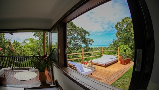 Una habitación con un ventanal grande que da a una terraza de madera con una cama y una mesita.