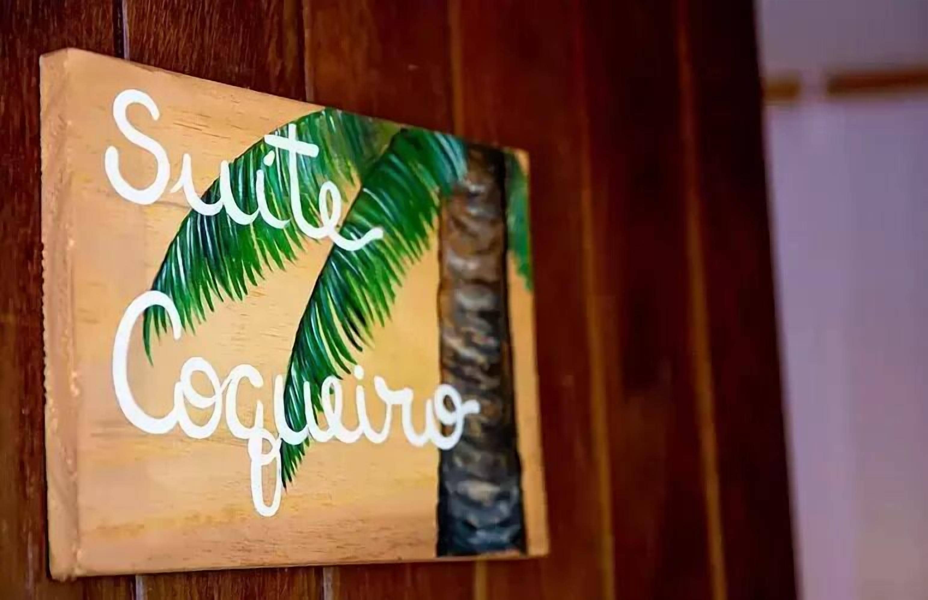 Un letrero de madera con el texto 'Suite Coqueiro' y un diseño de palmera.
