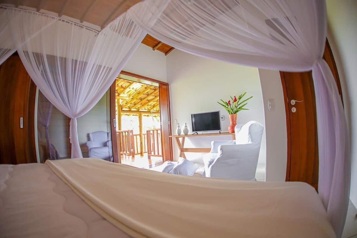 A bedroom with a bed, a TV, a plant, and a desk with chairs.