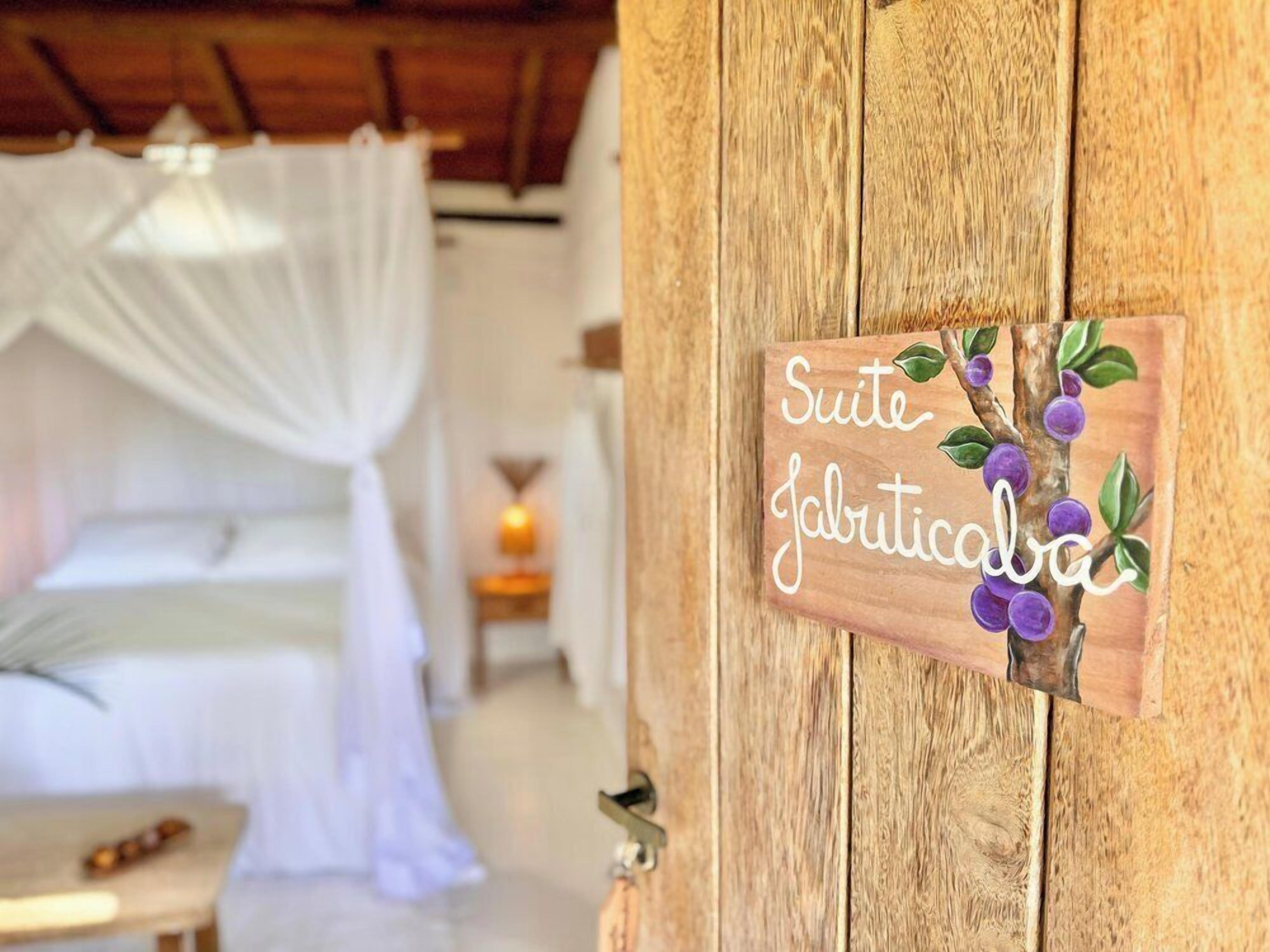 A wooden door with a sign that reads "Suite Jafriticaba" and a decorative branch with purple flowers.