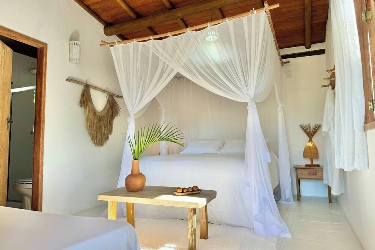 A room with a bed under a canopy, a small table with a plant, and a rustic wooden ceiling.
