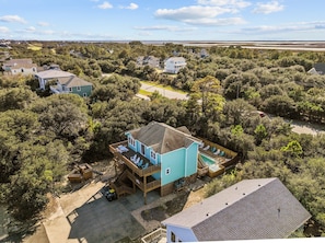 A two-story house with a pool and a deck, surrounded by dense trees and a coastal view.