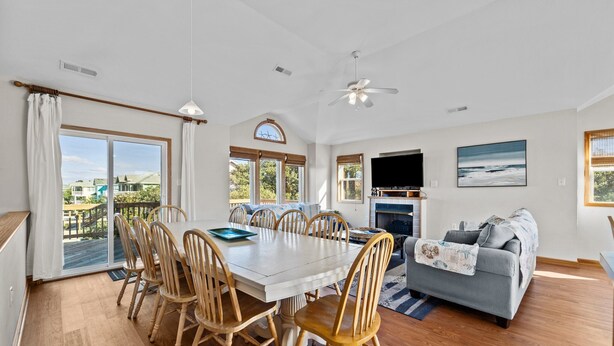 A spacious living room with a dining area, a gray sofa, and a TV. - Family Fun House! Private Pool, Putting Green, Walk to Beach, Hot Tub, Game Room (Corolla)