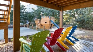 A wooden deck with colorful Adirondack chairs and a wooden play structure with a slide. - Family Fun House! Private Pool, Putting Green, Walk to Beach, Hot Tub, Game Room (Corolla)