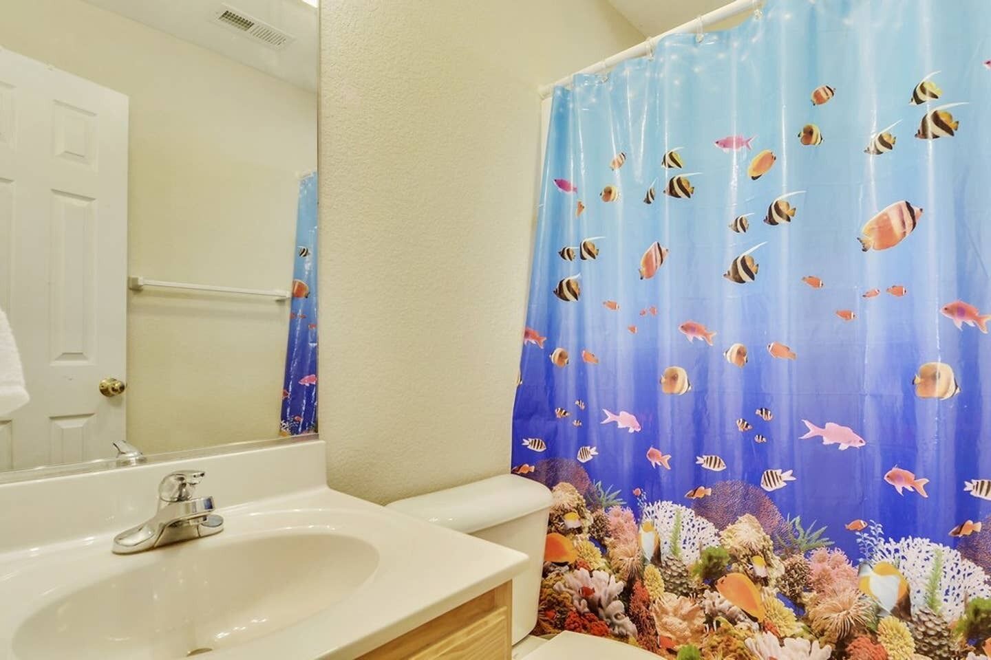 Un bagno con un lavandino bianco, uno specchio e una tenda da doccia con decorazioni a tema marino.