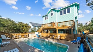 A two-story house with a swimming pool, deck chairs, and a wooden fence. - Family Fun House! Private Pool, Putting Green, Walk to Beach, Hot Tub, Game Room (Corolla)
