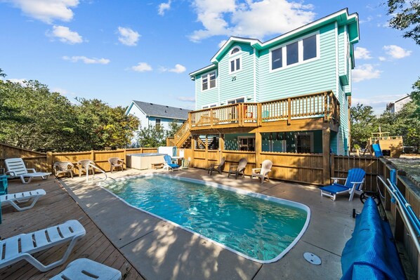 A two-story house with a swimming pool, deck chairs, and a wooden fence.