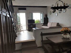 Una sala de estar con televisor, un sofá, una mesa de comedor con un jarrón de flores y una escalera que lleva a un espacio al aire libre.
