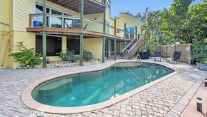 Una casa a due piani con piscina, area salotto esterna e terrazza in legno.