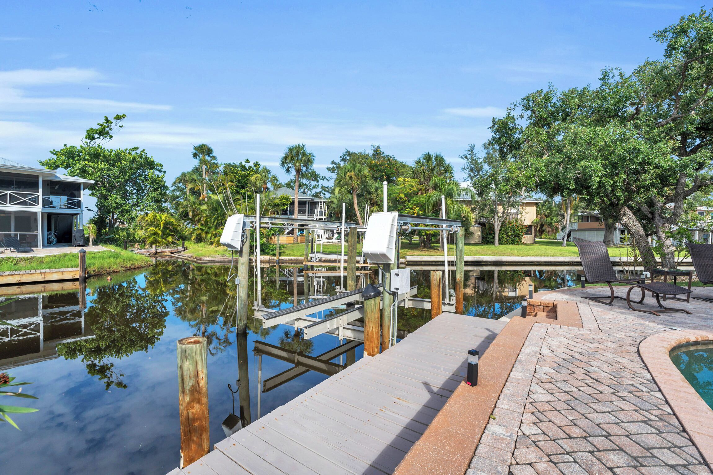 A dock extending over a calm water body with a wooden walkway and a pool area with lounge chairs.