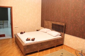 A wooden bed with white linens and two pillows, a wooden headboard, and a patterned wall.